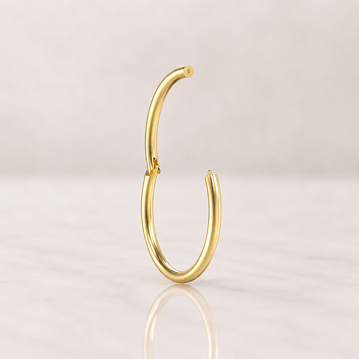 Clicker anneau en titane doré 1,2 x 6 mm ouvert, charnière visible, posé sur marbre clair