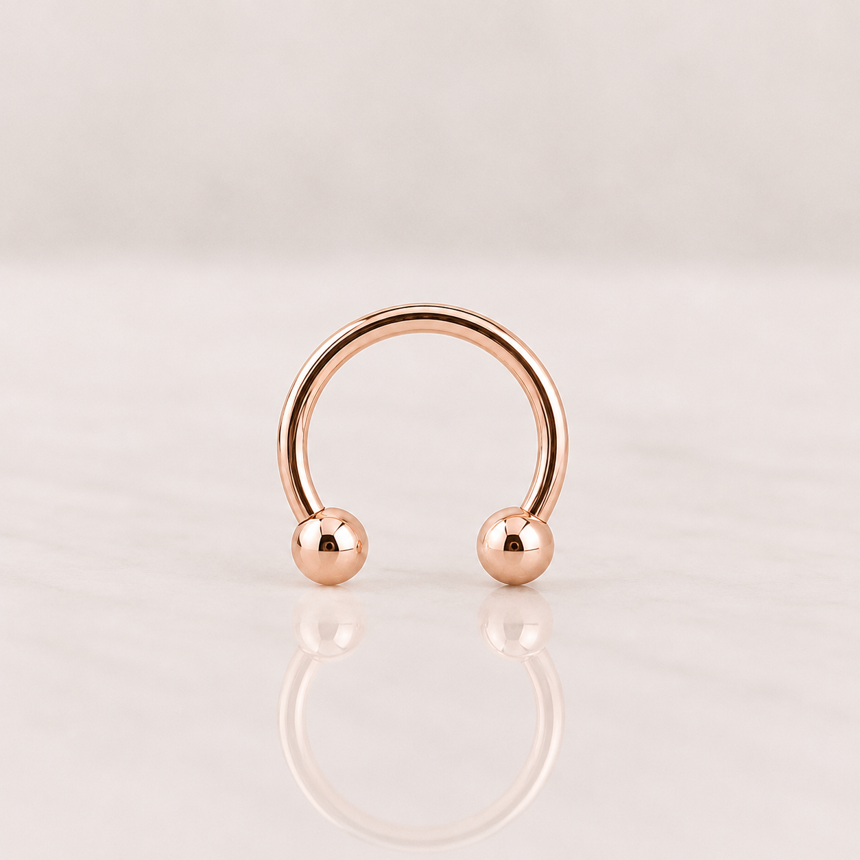 Circulaire fer à cheval en acier rose gold avec deux boules de 3 mm, posé sur fond clair