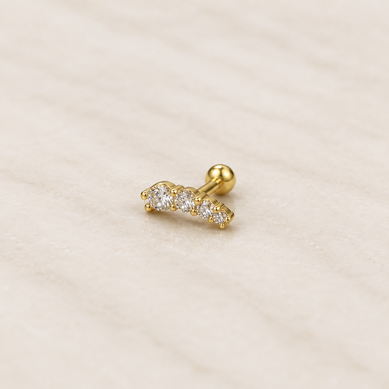 Labret acier doré avec barrette courbe de quatre zircons blancs et bille vissée, posé sur fond beige