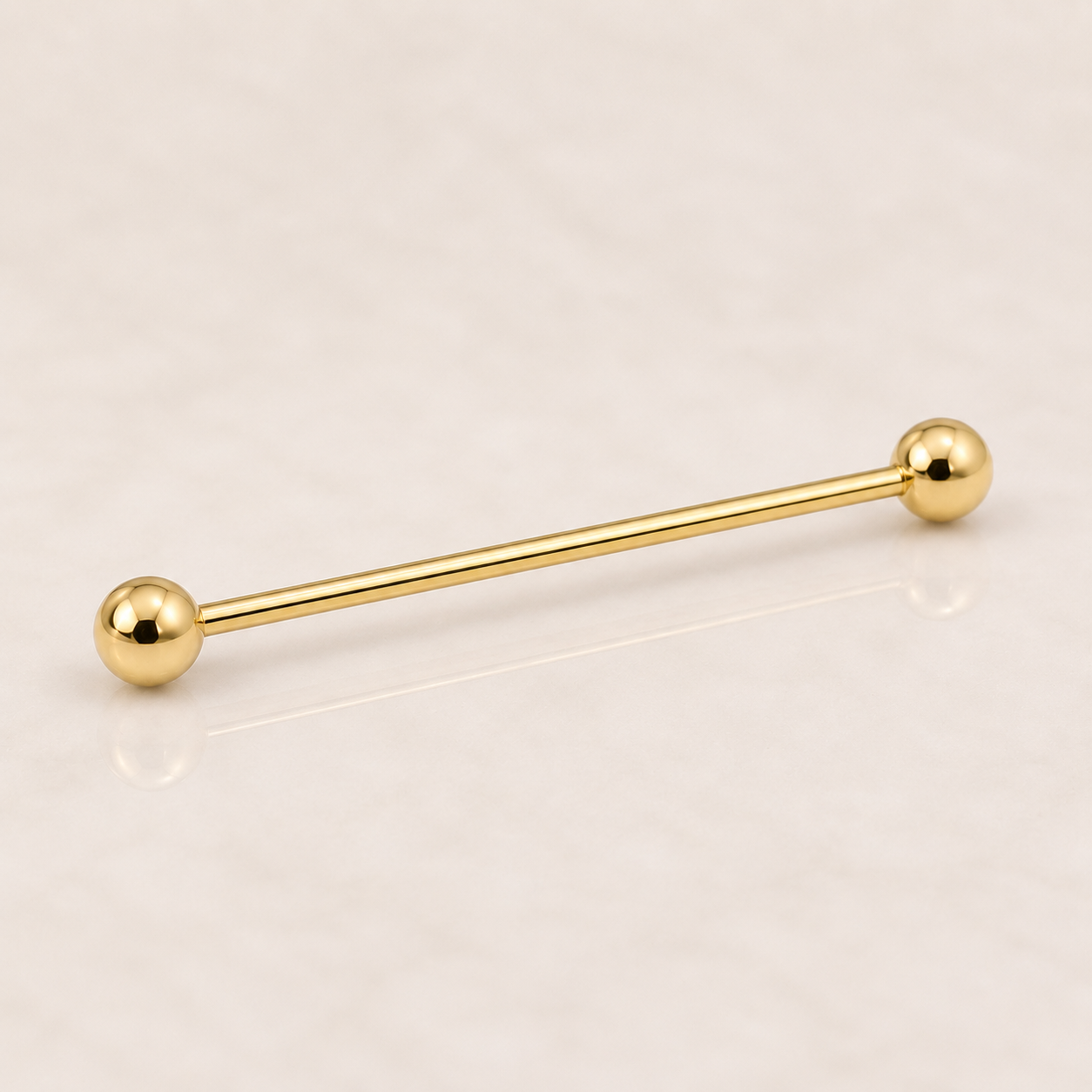 Barre industrielle en titane doré 1,6 x 34 mm avec deux boules de 4 mm, posée sur fond beige