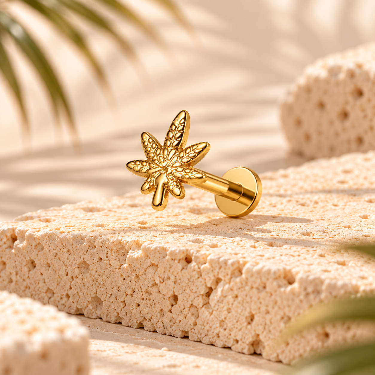 Stud flat back titane doré en forme de feuille ciselée, tige 1,2 mm et disque plat, posé sur pierre claire