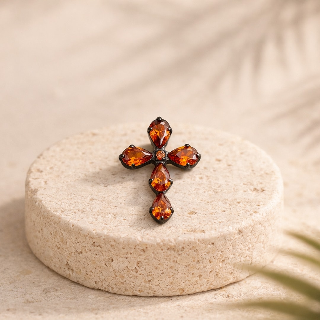 Stud flat back en titane noir en forme de croix sertie de zircons rouges poire, posé sur une pierre claire