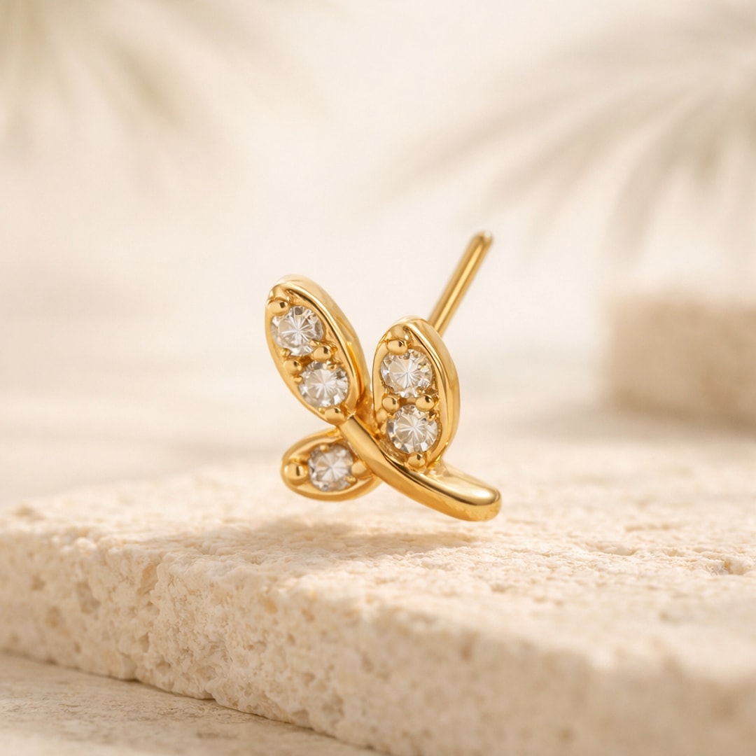 Nose stud papillon en acier doré serti de quatre zircons blancs, tige droite, posé sur une pierre claire