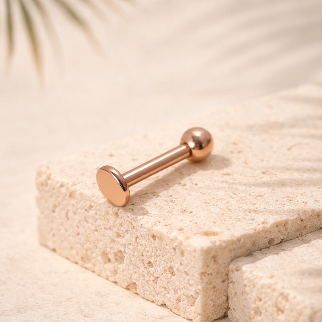 Labret droit en titane finition or rose, disque plat d'un côté et bille lisse de l'autre, posé sur une pierre claire