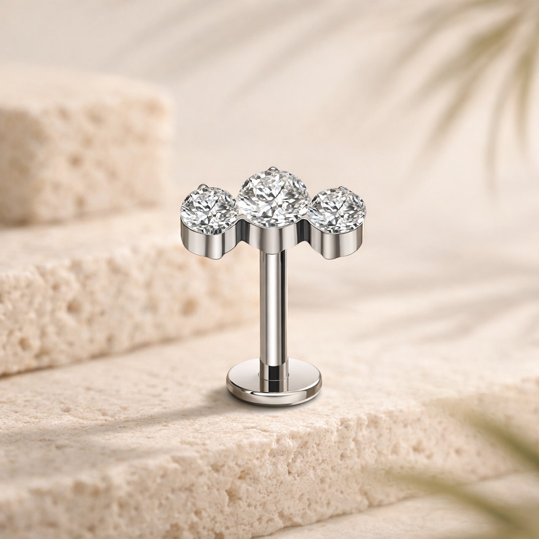 Stud flat back en titane argenté orné de trois zircons blancs alignés, posé sur une pierre claire