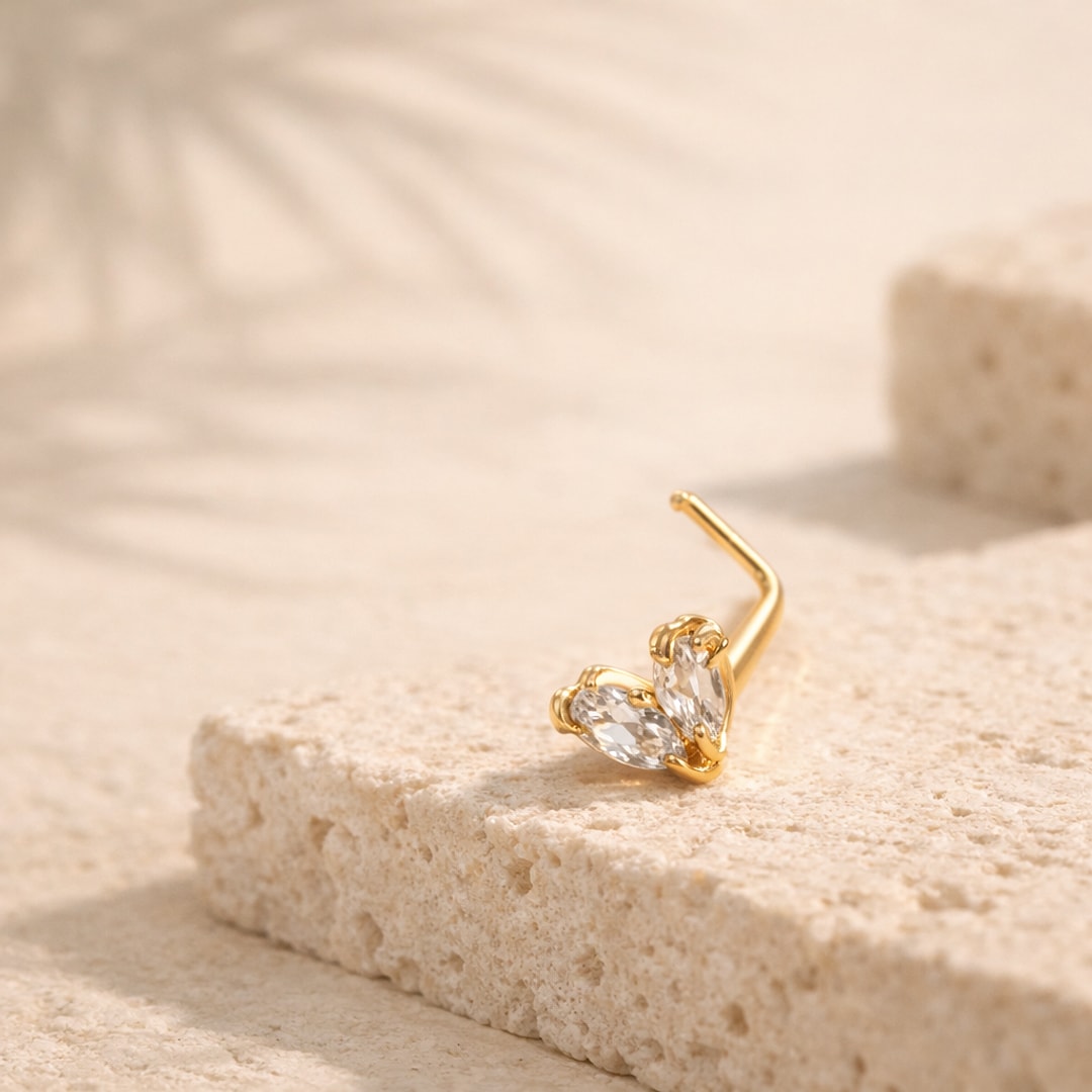 Stud de nez doré à tige en L avec deux zircons blancs taille marquise, posé sur une pierre claire