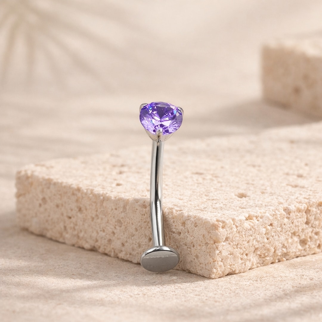 Banane de nombril en titane argenté avec zircon rond violet serti griffes, posée sur une pierre claire