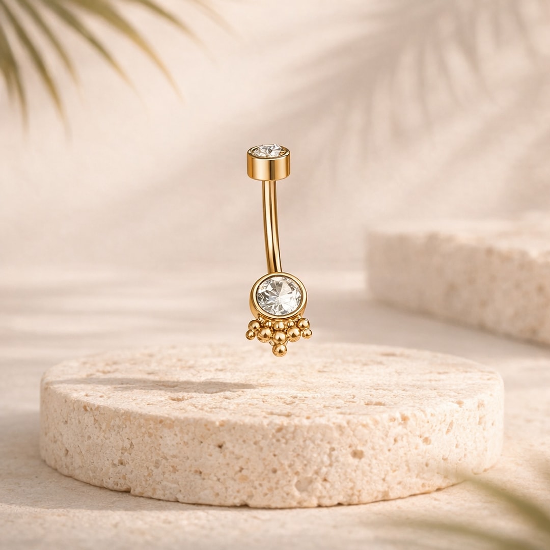 Banane de nombril dorée avec deux pierres cristal rondes et grappe de billes, posée sur pierre beige