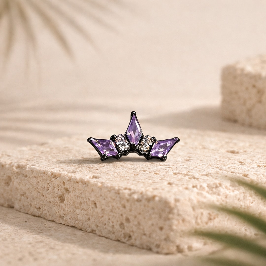 Stud flat back en titane noir en forme de couronne, zircons violets et blancs, posé sur une pierre claire