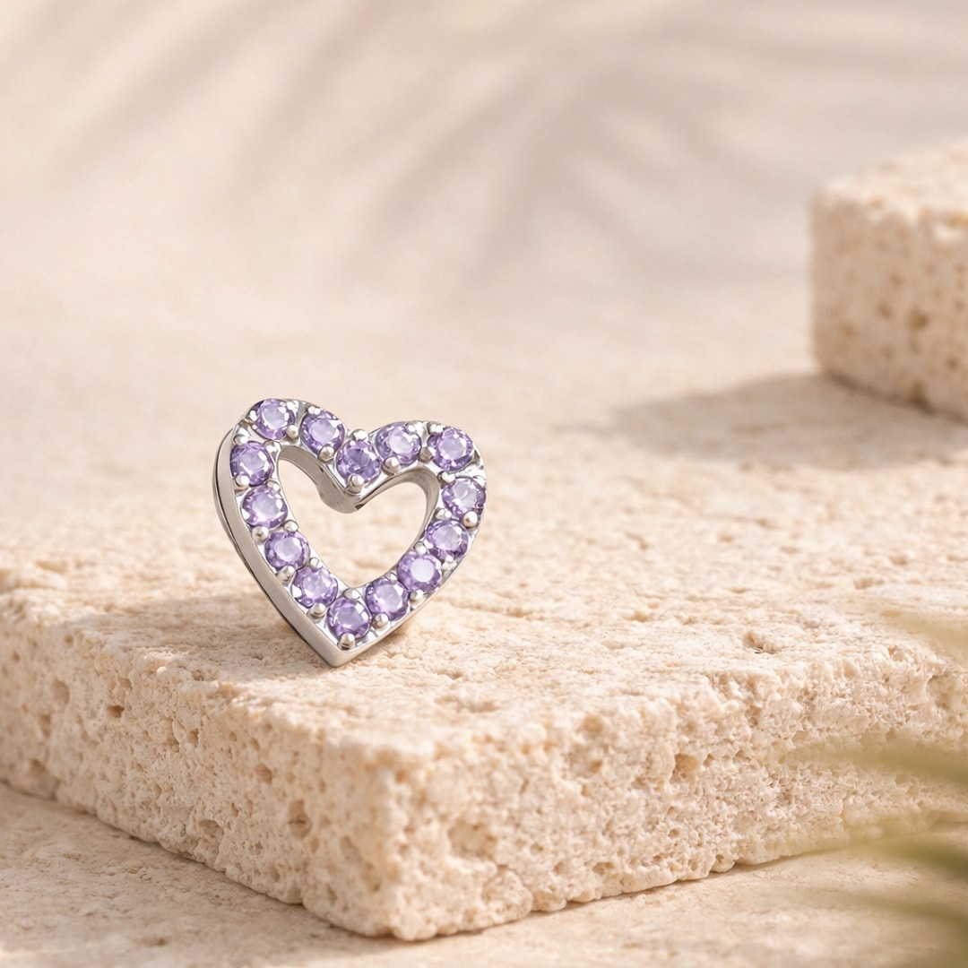 Top de piercing en forme de cœur ajouré en titane argenté serti de zircons violets, posé sur une pierre claire