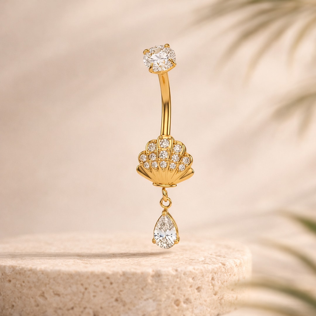Banane de nombril dorée avec coquillage serti de zircons et goutte pendante, posée sur pierre claire