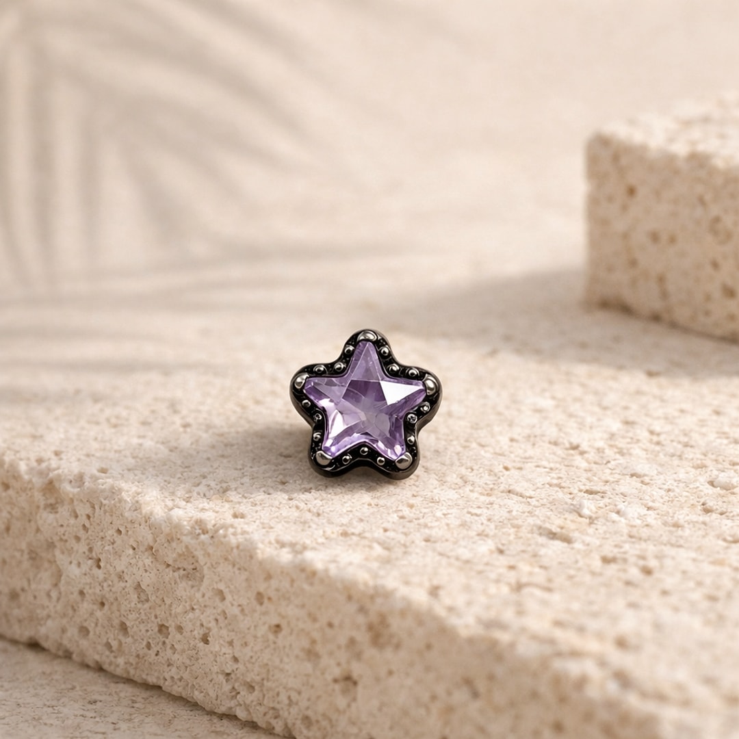 Stud flat back en titane noir orné d'une étoile zircon violet, posé sur une pierre claire