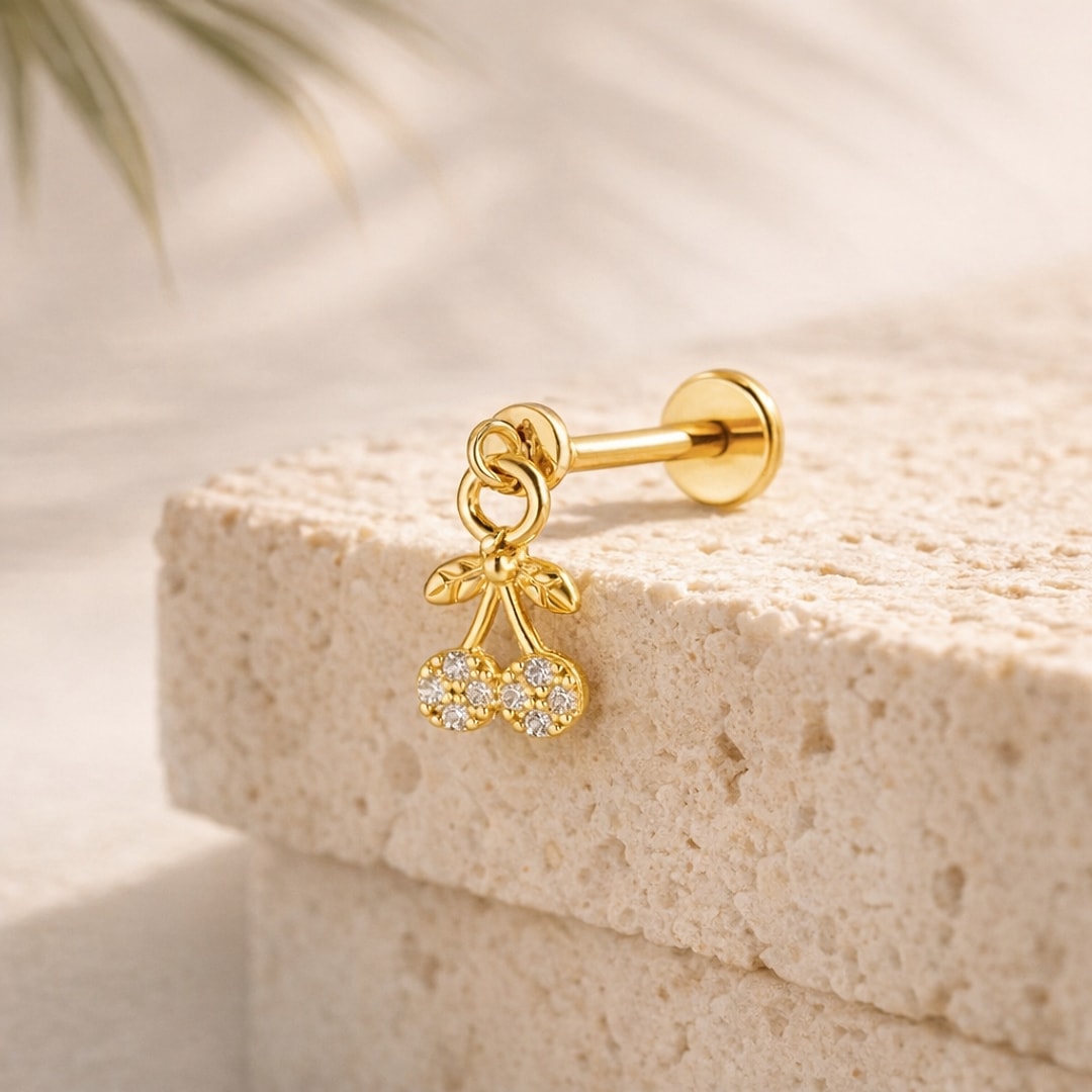 Stud flat back doré avec pendentif cerise serti de cristaux, posé sur une pierre beige