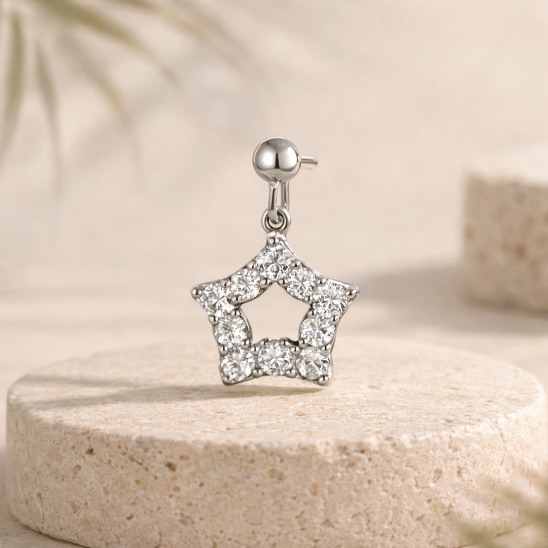 Stud piercing en acier argenté avec étoile pendante sertie de zircons, posé sur une pierre beige