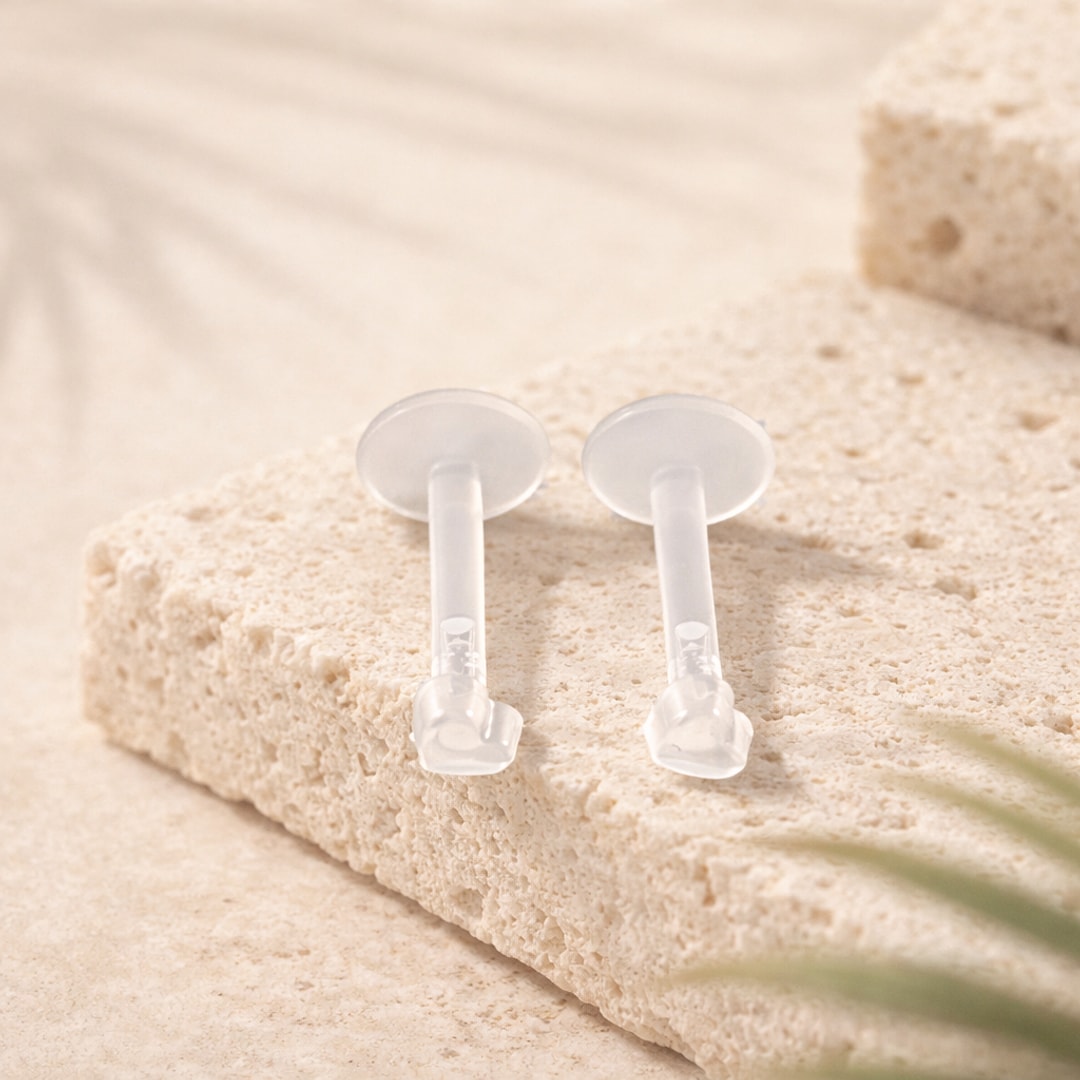 Deux rétainers labret en acrylique transparent, disque plat et tête à pression, posés sur une pierre claire