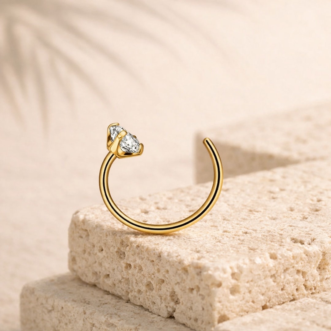 Nose stud courbé en titane doré avec zircon blanc en forme de goutte, posé sur une pierre claire
