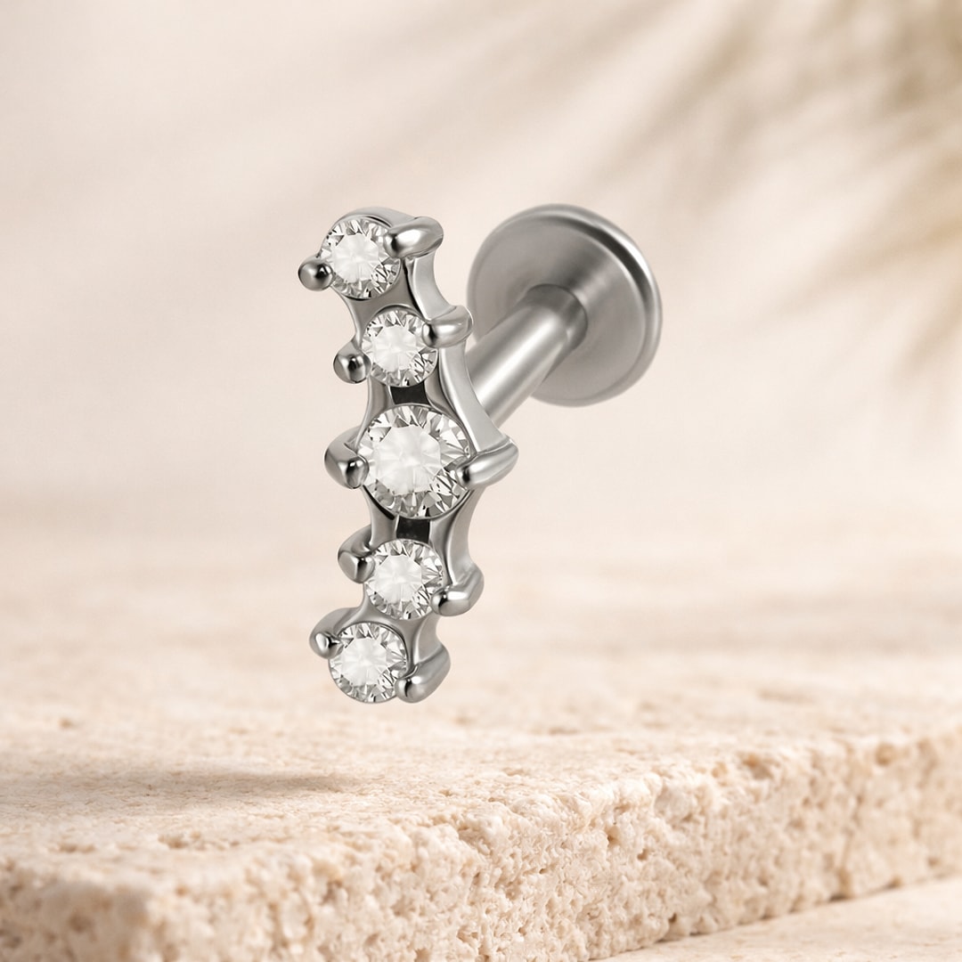 Labret acier argenté avec cinq cristaux ronds alignés et disque plat, posé sur pierre beige