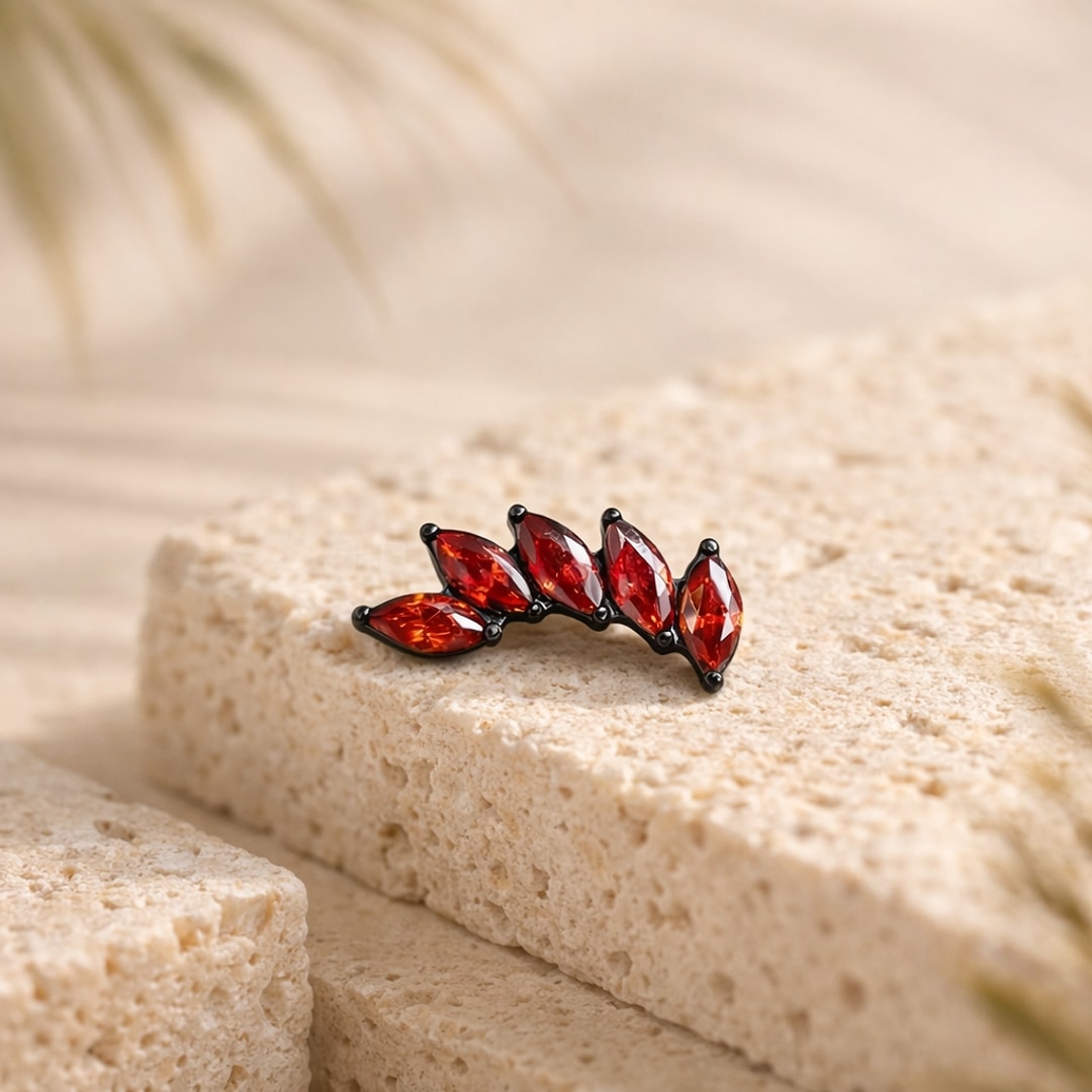 Stud flat back en titane noir avec quatre zircons rouges taille marquise en forme de feuilles, posé sur une pierre claire