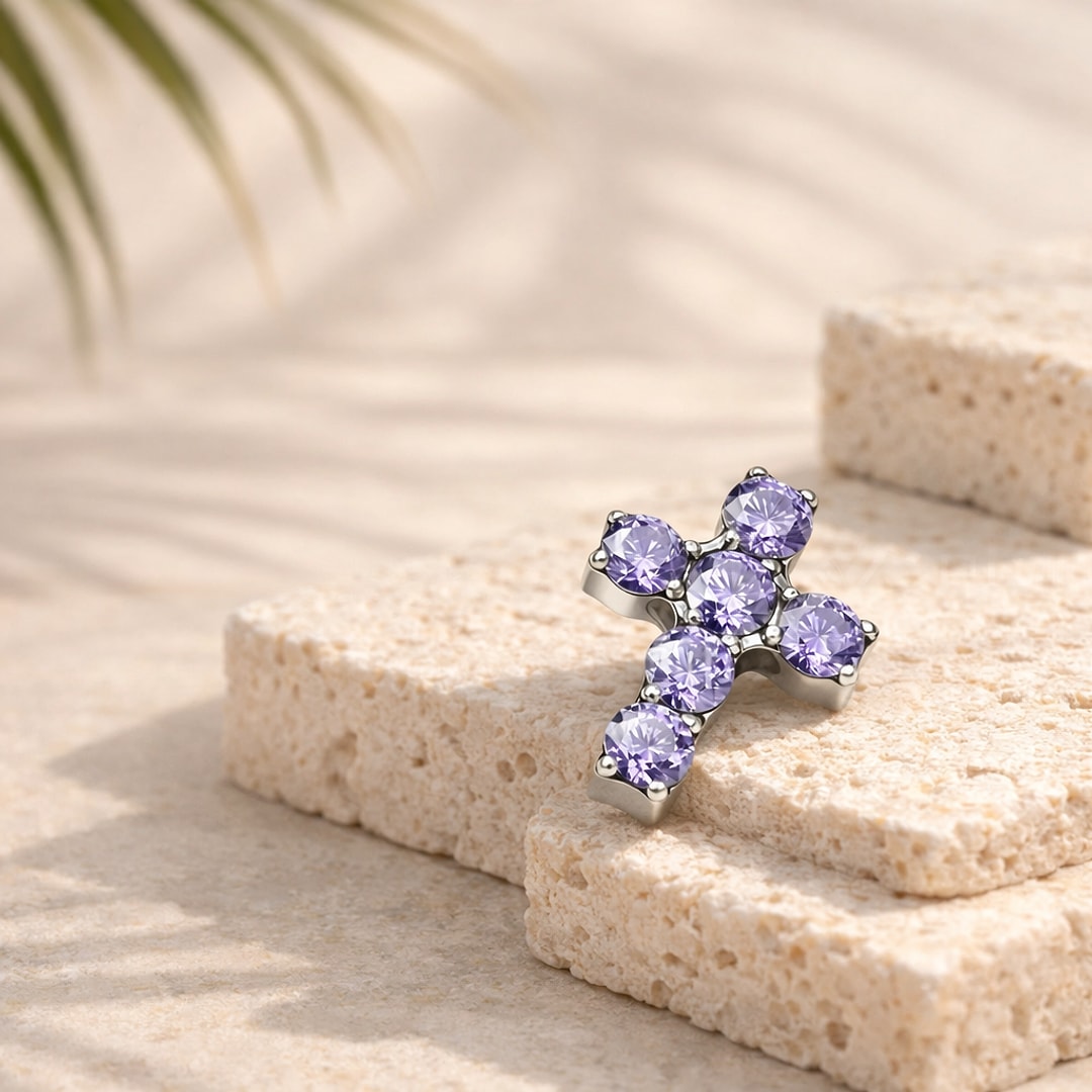 Top de piercing en titane argenté en forme de croix sertie de six zircons violets, posé sur une pierre claire