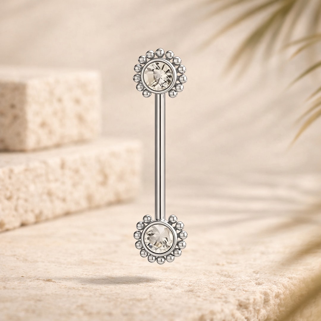 Barbell de téton en titane argenté avec embouts fleur sertis d'un zircon clair, posé sur pierre claire