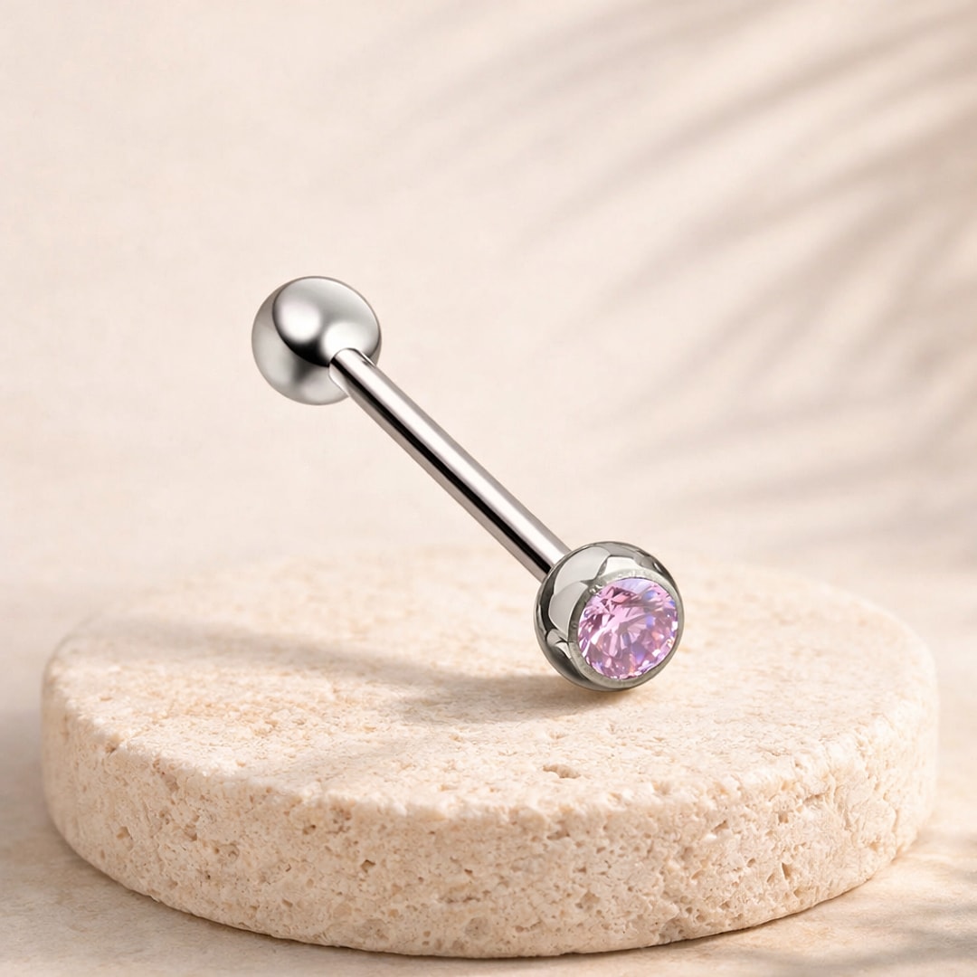 Barre de langue en titane argenté avec zircon cubique rose serti et bille lisse, posée sur une pierre claire