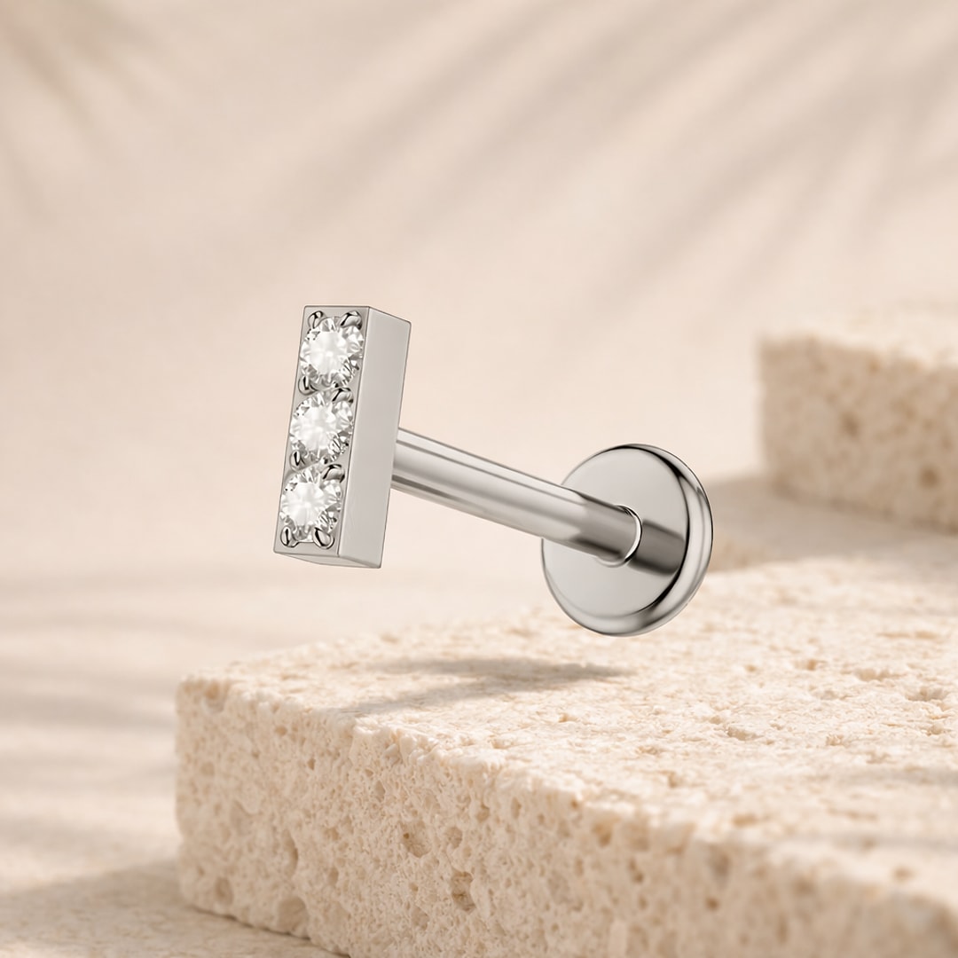 Labret acier argenté avec barrette sertie de trois pierres blanches et disque plat, posé sur pierre claire