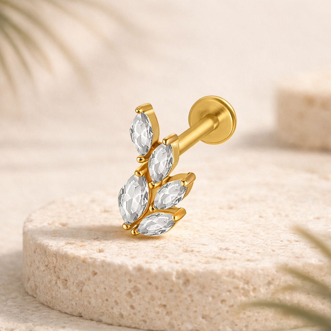Labret doré motif feuille avec cinq cristaux marquise blancs et tige à disque plat, posé sur une pierre claire