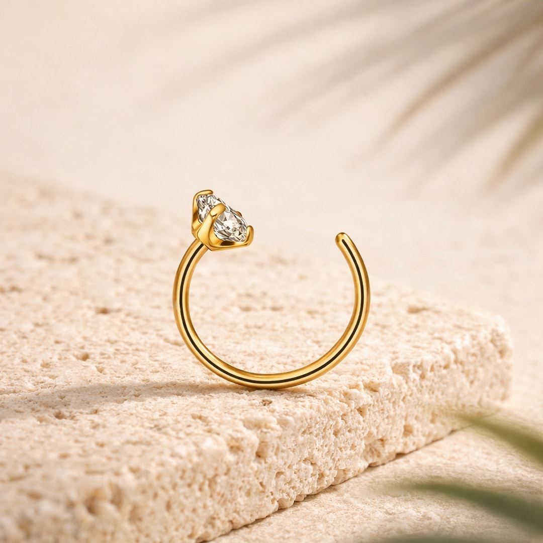 Anneau de nez ouvert en titane doré orné d'un zircon blanc taille goutte, posé sur une pierre claire