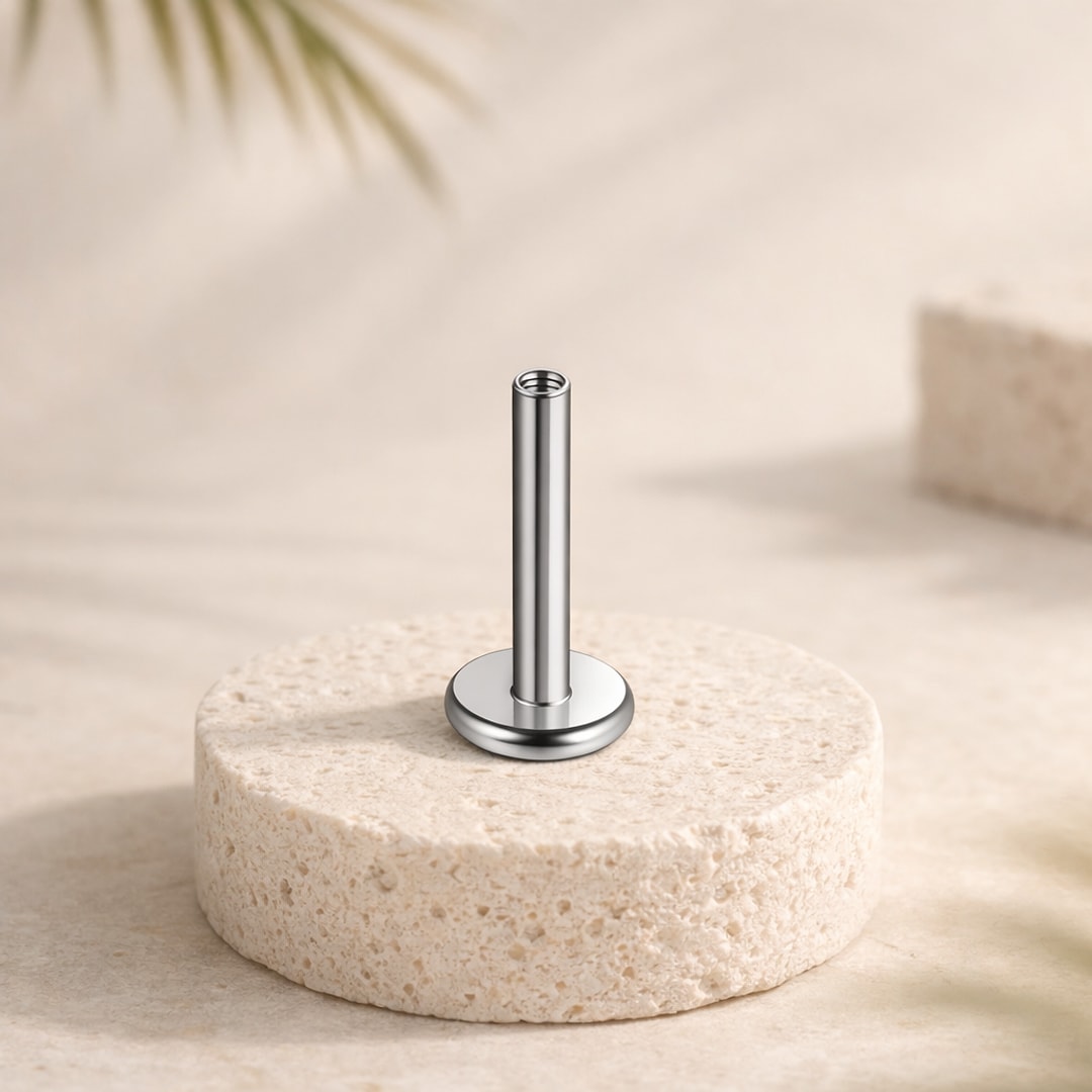 Base de labret flat back en titane argenté, tige droite à filetage interne et disque plat, posée sur une pierre claire