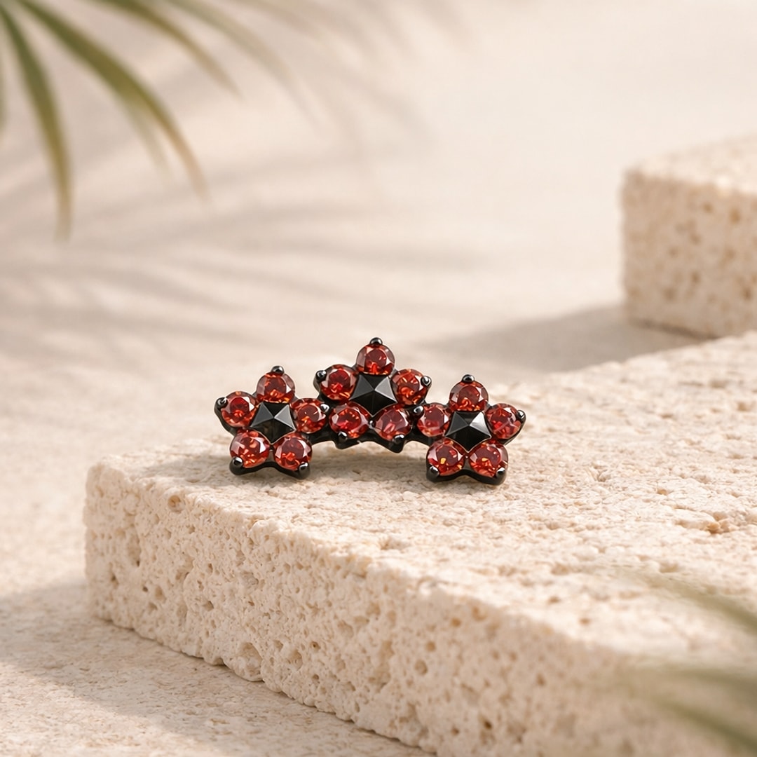 Stud flat back titane noir, trois fleurs de zircons rouges à centre noir, posé sur une pierre claire