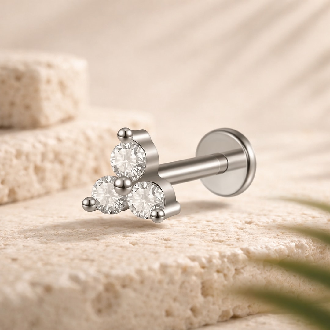Labret acier argenté avec trois cristaux ronds sertis en triangle et disque plat, posé sur une pierre claire