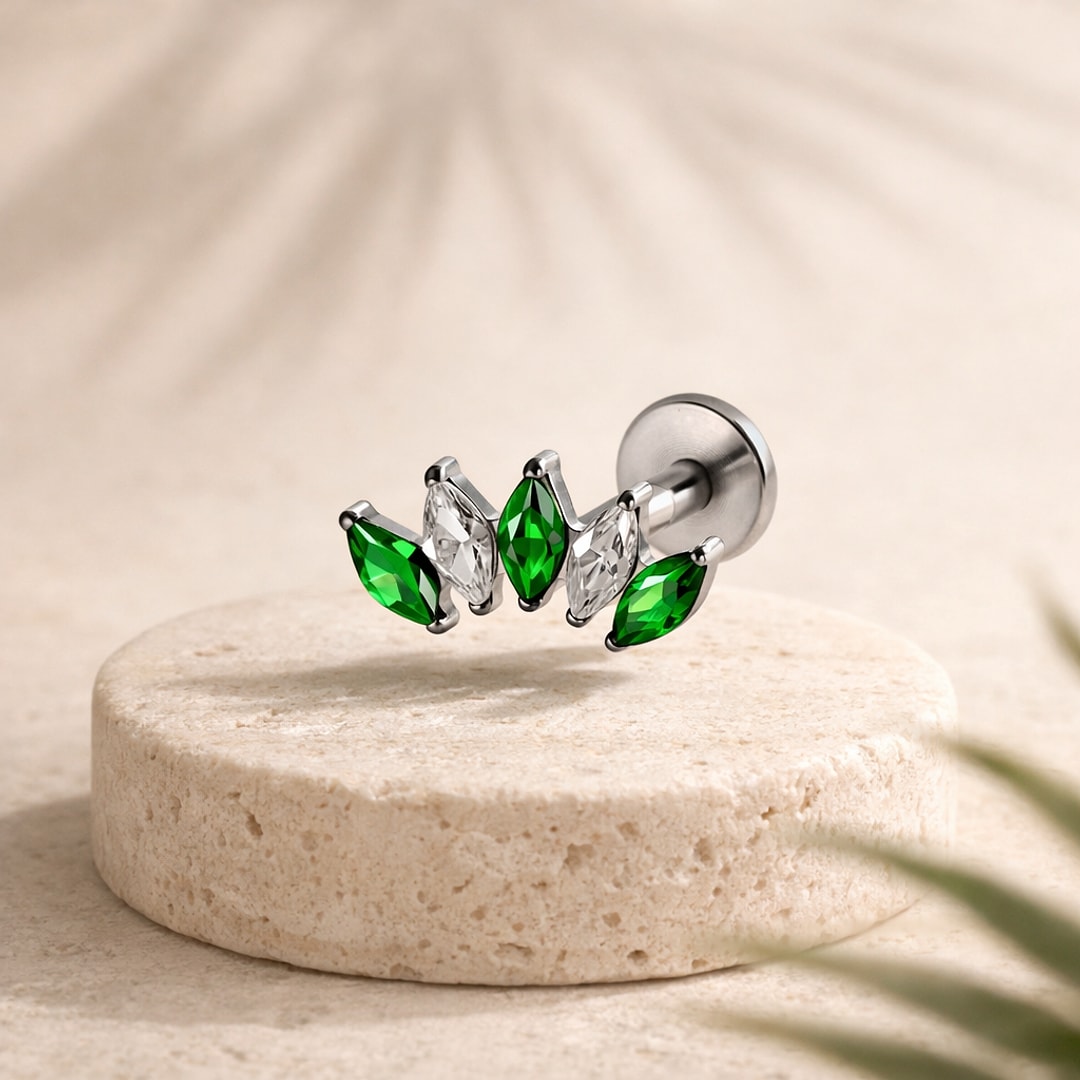 Labret flat back en titane argenté orné de cinq zircons marquise verts et blancs en éventail, posé sur une pierre claire