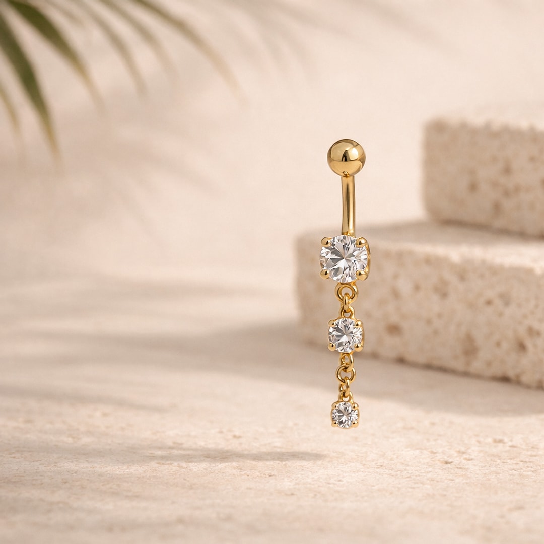 Banane de nombril dorée avec pendentif de trois zircons blancs sertis griffes, posée sur pierre claire