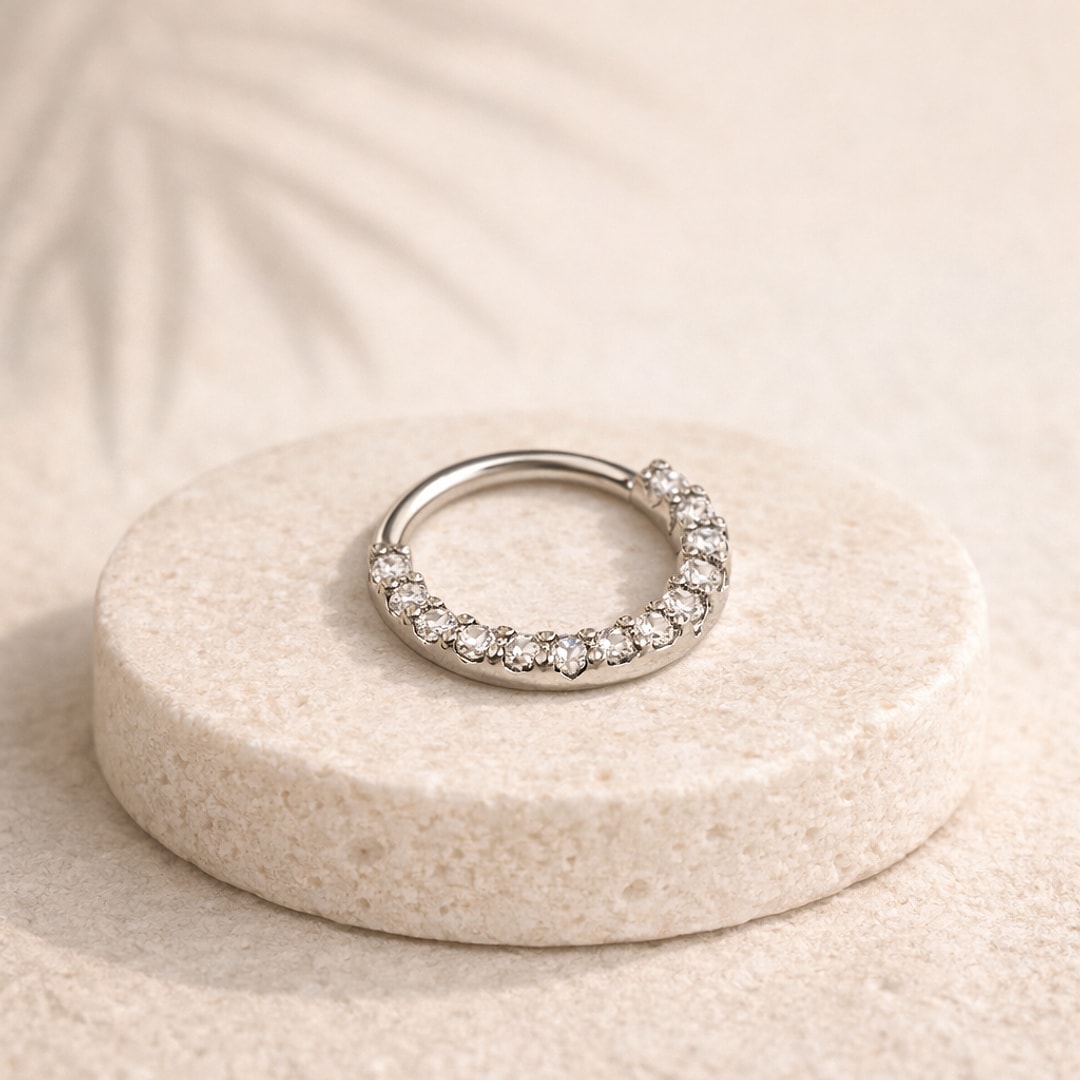 Anneau de nez clicker en acier argenté pavé de zircons blancs, posé sur un socle de pierre claire