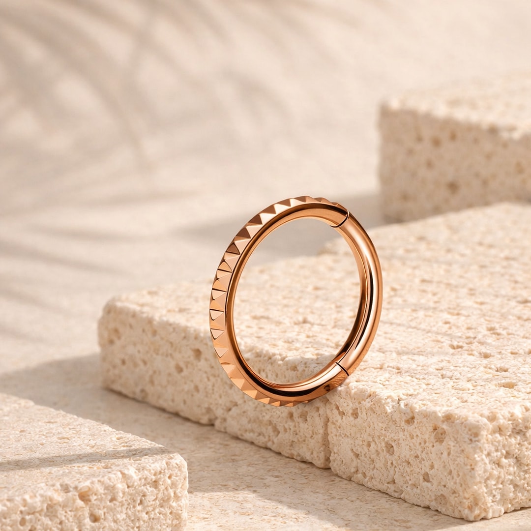 Anneau clicker en titane rose gold avec facettes pyramidales, posé sur une pierre claire