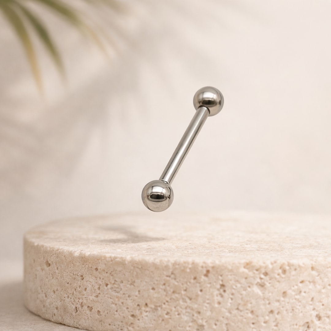 Barbell droit en titane argenté avec deux boules vissées, posé sur une pierre beige