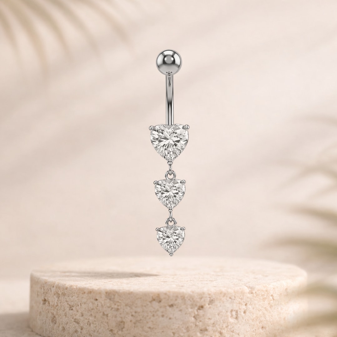 Piercing nombril acier argenté avec trois cœurs en zircon pendants sur une pierre beige