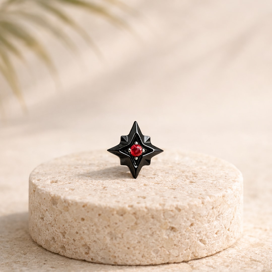 Stud flat back titane noir en forme d'étoile du Nord avec zircon rouge au centre, posé sur une pierre claire
