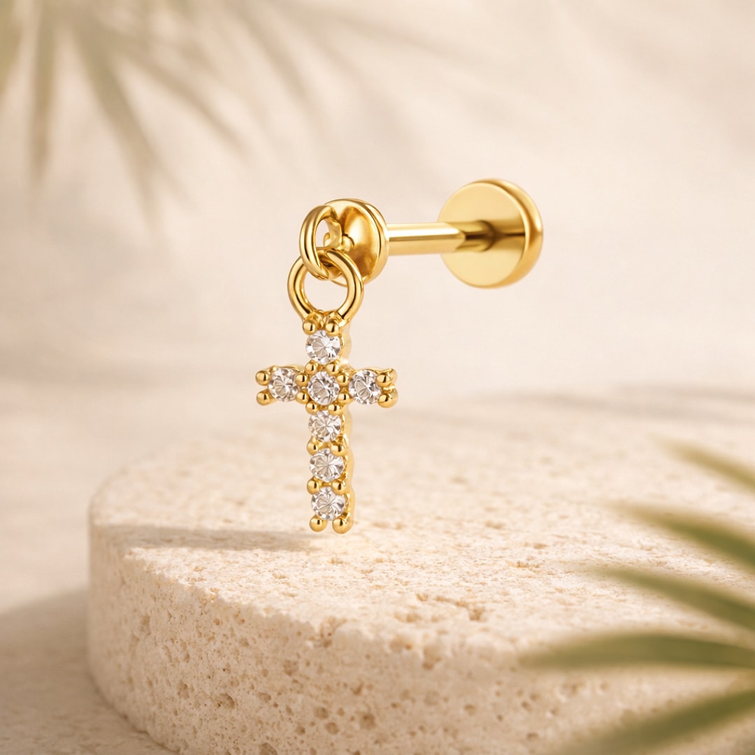 Stud flat back doré avec pendentif croix serti de pierres blanches, posé sur une pierre claire