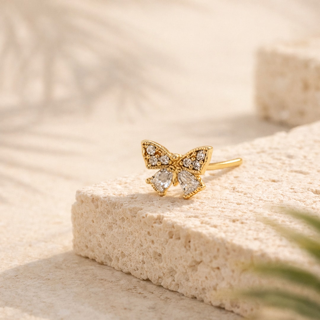 Nose stud papillon doré serti de zircons blancs, tige coudée en acier, posé sur une pierre claire