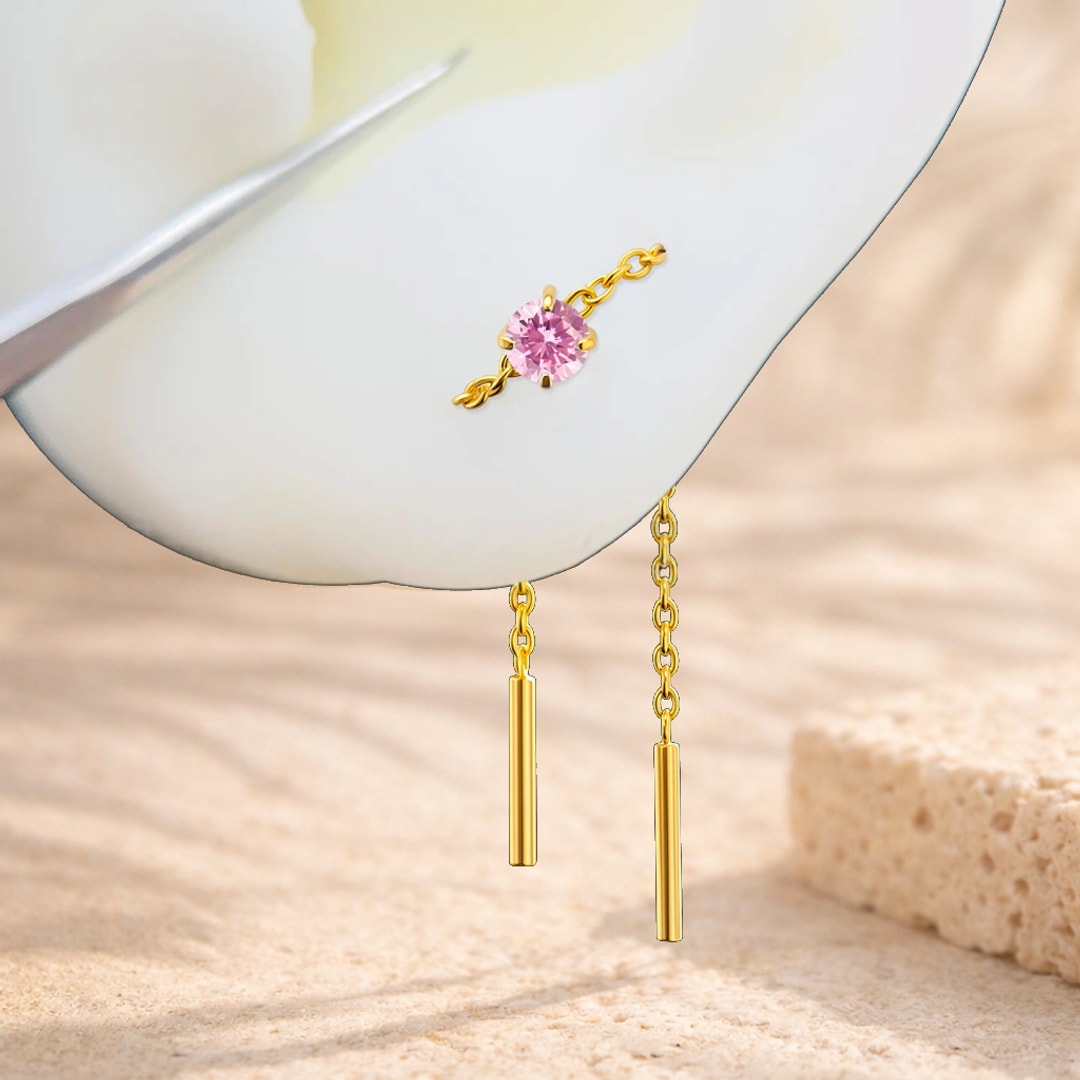 Chaîne d'oreille en titane doré avec zircon rose serti et barrette pendante, posée sur un pétale blanc