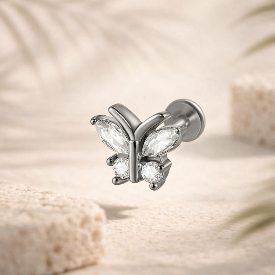 Labret papillon en acier argenté serti de zircons blancs, tige à disque plat, posé sur fond beige