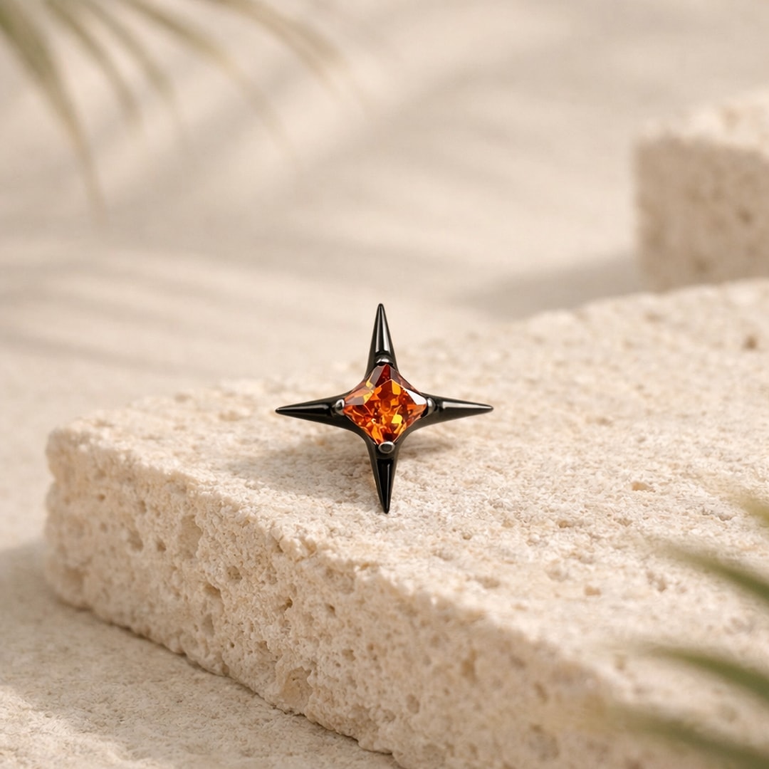 Stud flat back étoile à quatre branches en titane noir serti d'un zircon orange, posé sur une pierre claire
