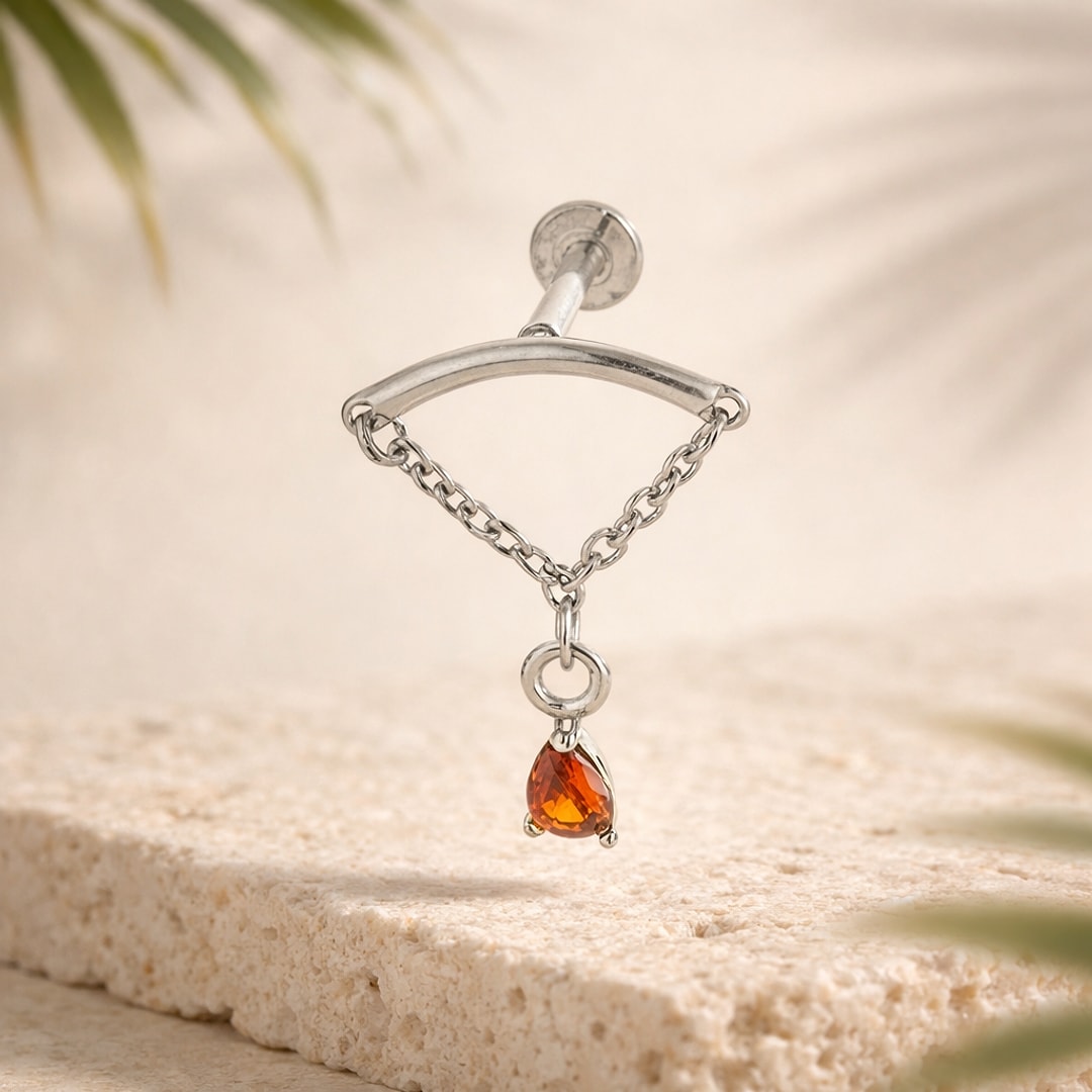 Labret acier argenté à chaînette fine et pendentif goutte zircon orange posé sur une pierre claire