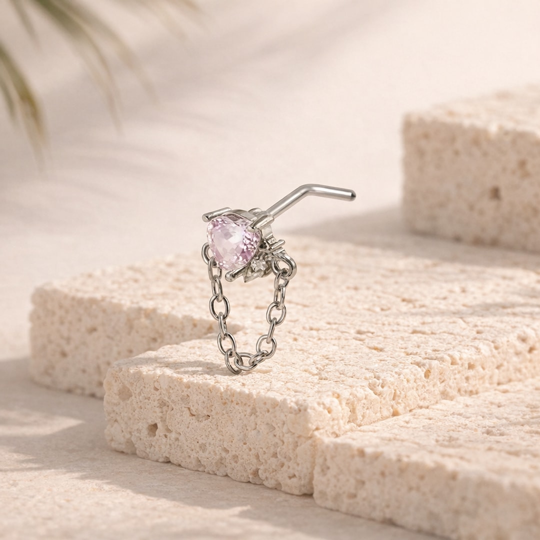 Stud nez en L argenté avec cœur en zircon rose et chaînette, posé sur une pierre claire