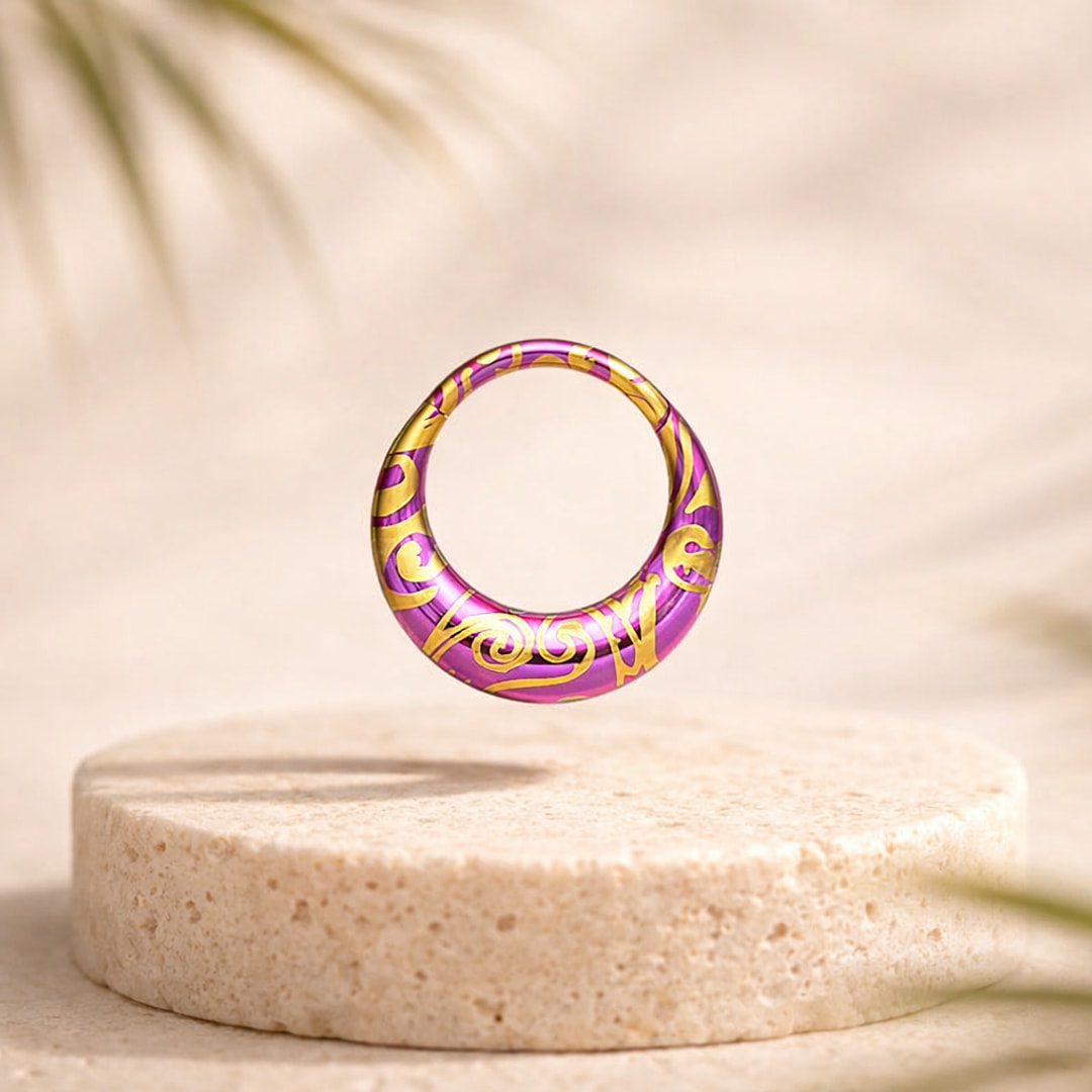 Bijou de piercing en titane anodisé violet orné de volutes dorées, posé sur un socle de pierre claire