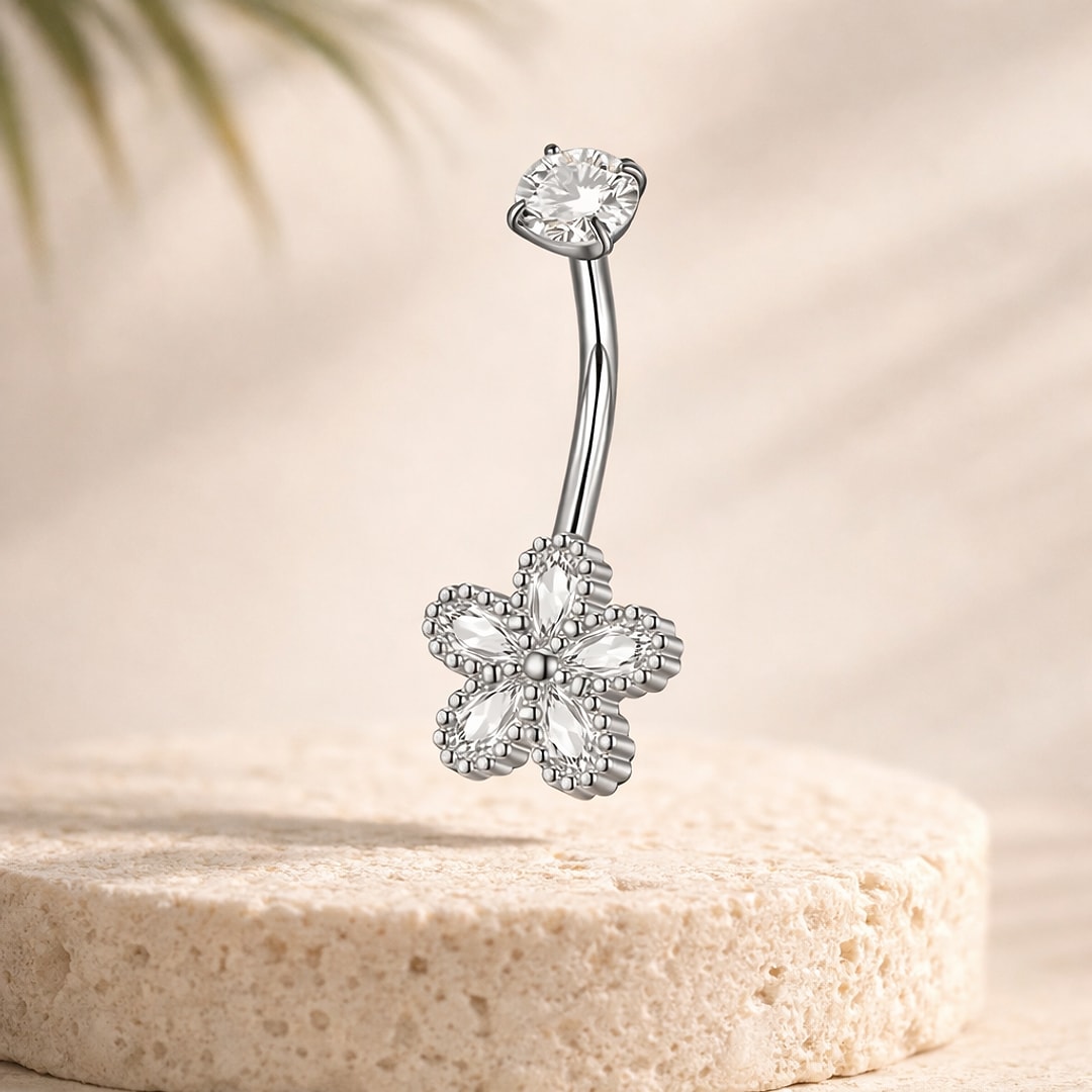 Piercing nombril acier argenté avec fleur en cristaux blancs et pierre ronde, posé sur une pierre claire