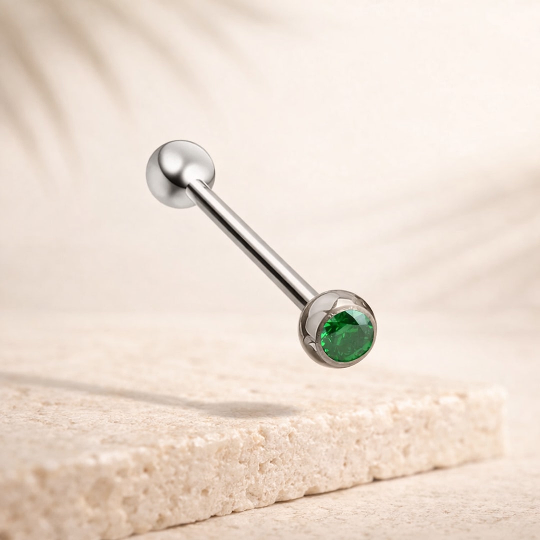 Barre de langue en titane avec zircon rond vert serti clos et bille lisse, posée sur pierre claire