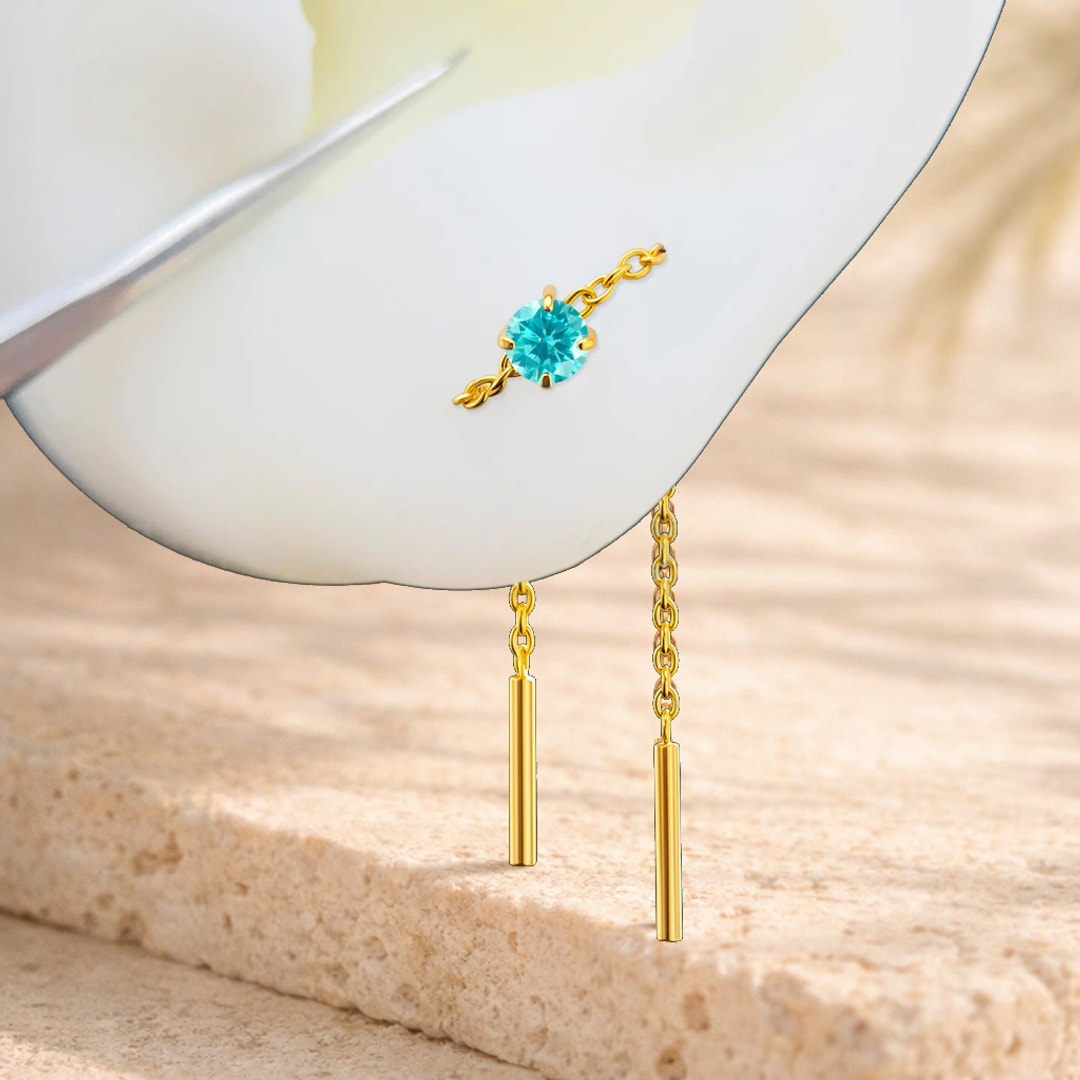 Chaîne d'oreille en titane doré avec zircon bleu et barrette pendante posée sur un pétale blanc
