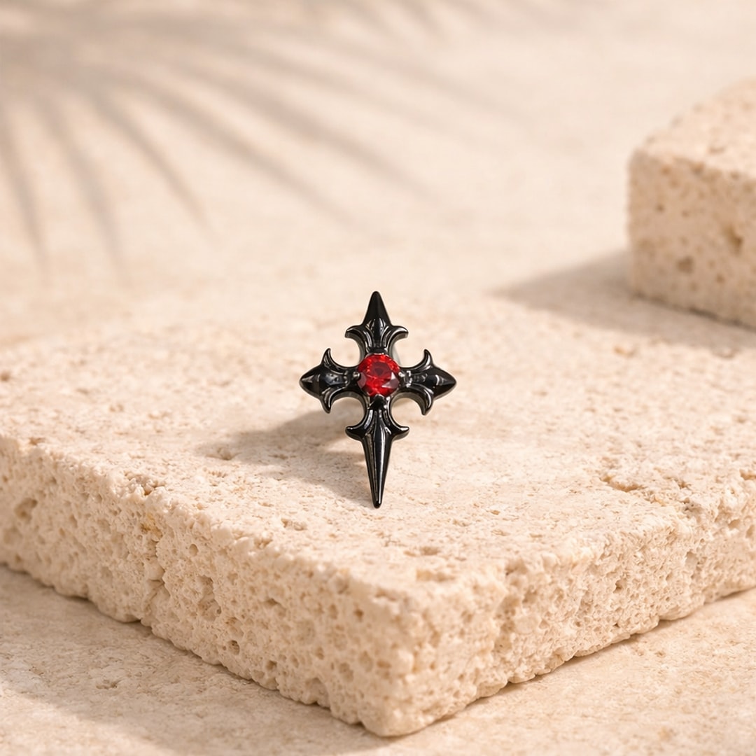 Stud flat back en titane noir en forme de croix gothique avec zircon rouge au centre, posé sur une pierre claire